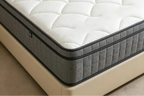 Close-up of a mattress with quilted design and brand logo on a beige bed frame.